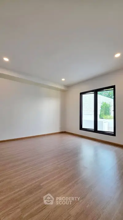 Spacious empty room with wooden flooring and large windows, perfect for customization.
