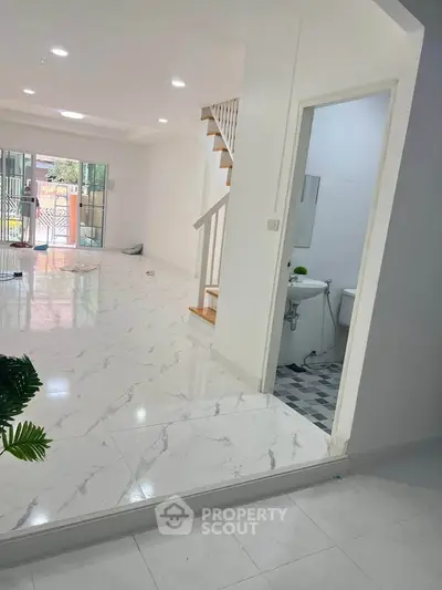 Spacious modern living area with marble flooring and staircase, adjacent to a compact bathroom.