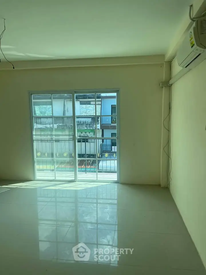Spacious living room with large windows and balcony access, offering ample natural light and modern air conditioning.