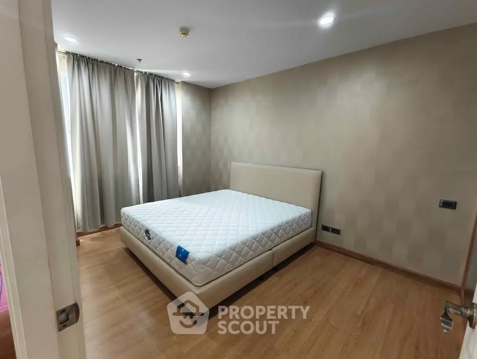 Spacious bedroom with modern design and natural light, featuring a comfortable bed and elegant curtains.