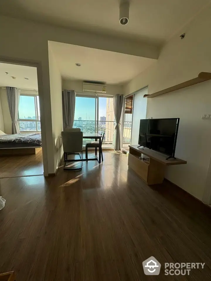 Modern apartment with open living area and city view, featuring sleek wooden flooring and natural light.