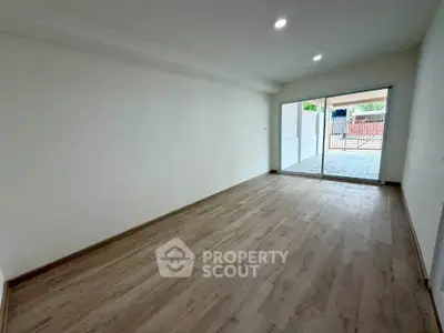 Spacious empty room with wooden flooring and large sliding glass doors leading to a patio.