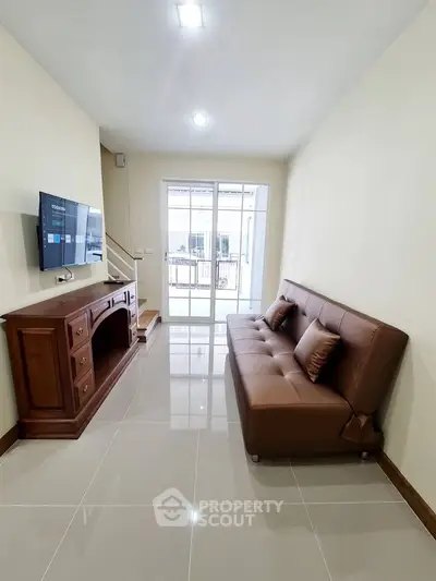 Modern living room with sleek sofa and wall-mounted TV, bright natural light from large windows.