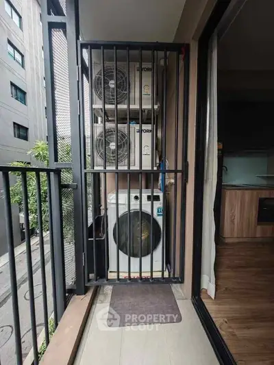 Compact balcony with washing machine and air conditioning units in modern apartment.