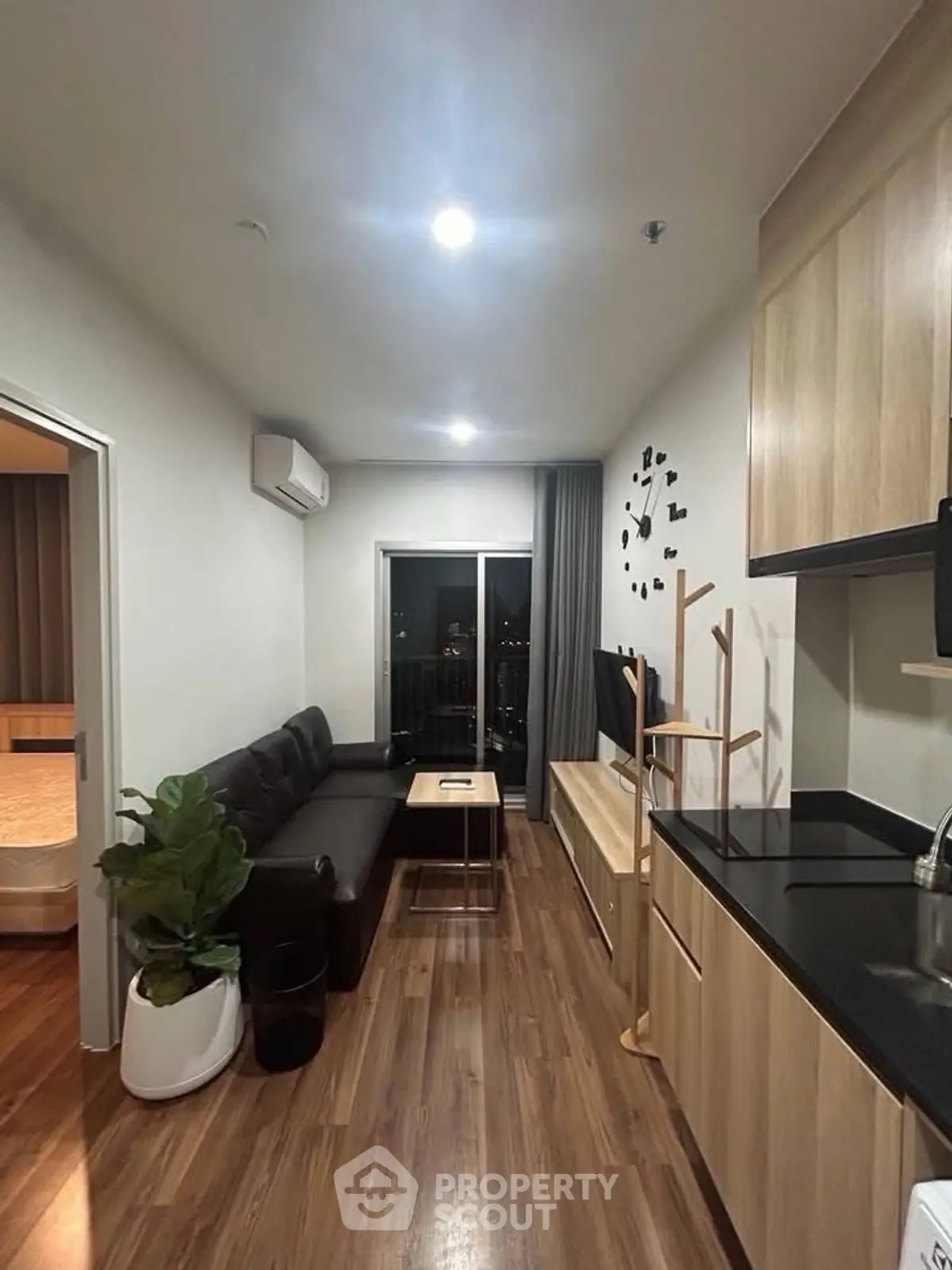 Modern living room with sleek kitchen and cozy seating area, featuring wooden flooring and stylish decor.