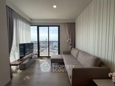 Modern living room with large windows and city view, featuring a comfortable sofa and sleek TV setup.