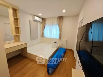 Modern bedroom with wooden flooring, built-in desk, and wall-mounted TV in a cozy apartment.