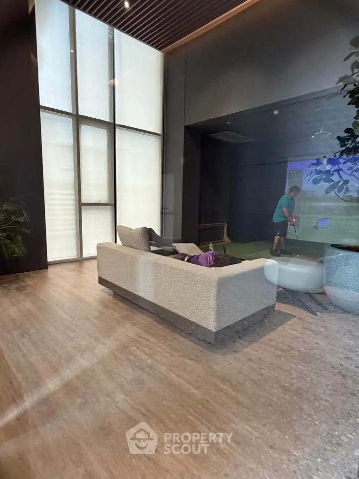 Luxurious modern living room with high ceilings and large windows, featuring a cozy sofa and indoor golf simulator.