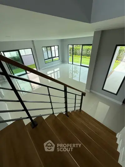 Spacious modern living room with large windows and wooden staircase, offering abundant natural light and garden view.