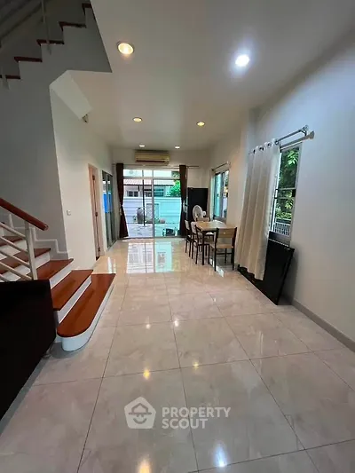 Spacious open-plan living area with modern staircase and dining space, featuring large windows for natural light.