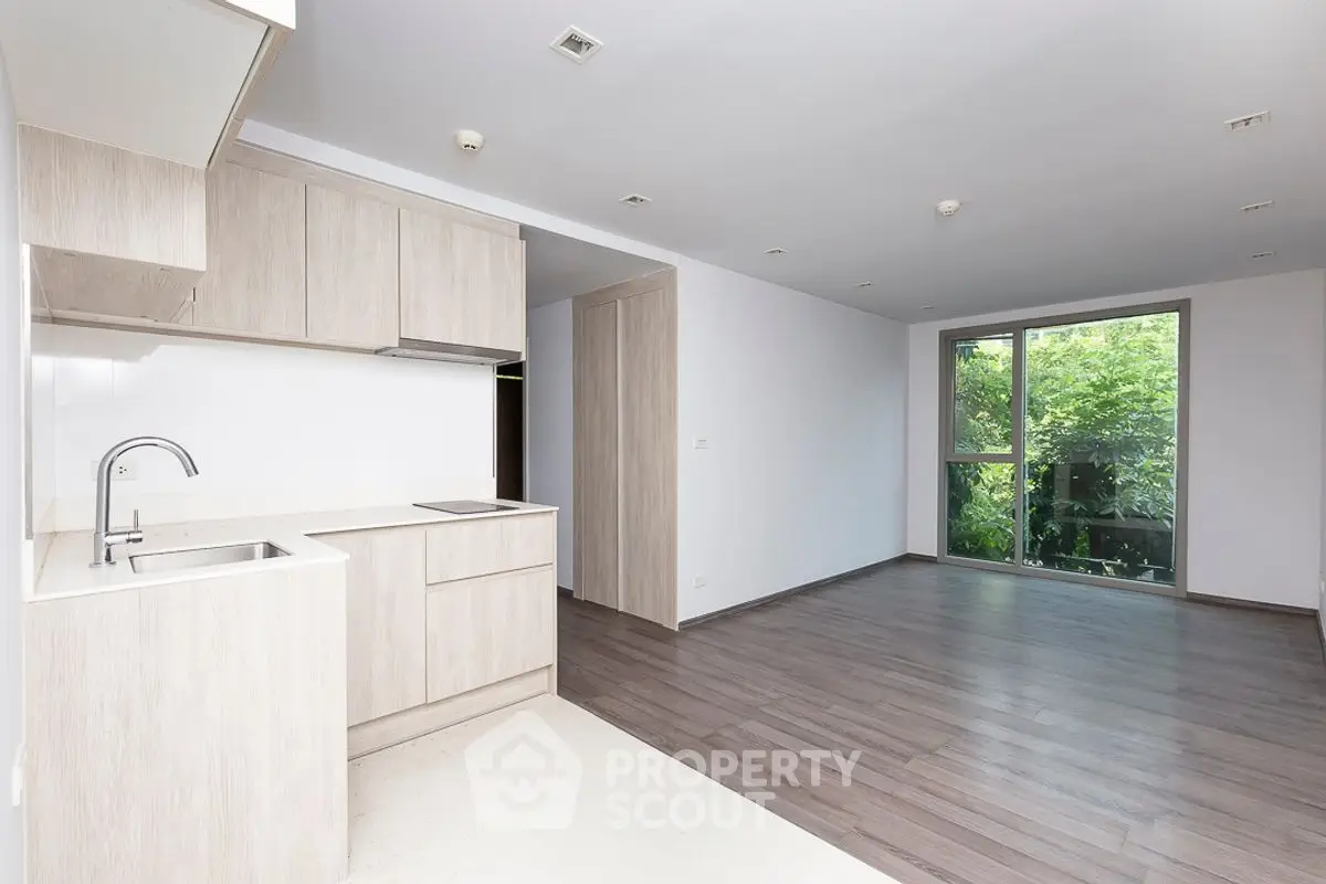 Modern open-plan kitchen and living area with large window and wooden flooring.