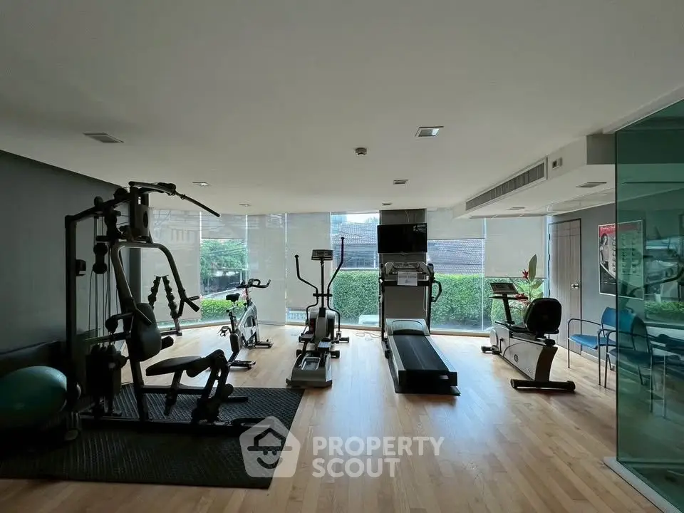 Spacious gym with modern equipment and large windows in a residential building.