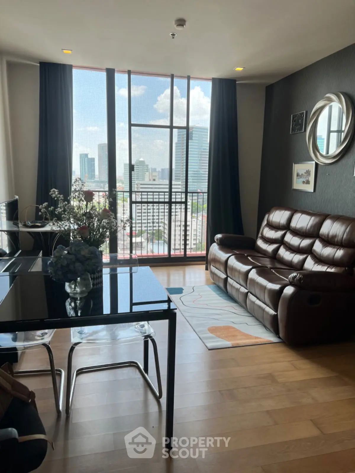 Modern living room with city view, leather sofa, and dining area in a high-rise apartment.