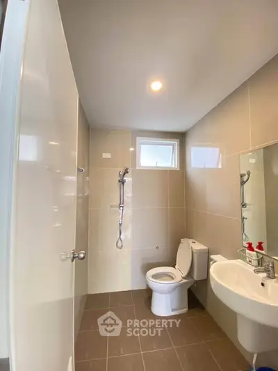 Modern bathroom with sleek fixtures and neutral tiles, featuring a shower and toilet.