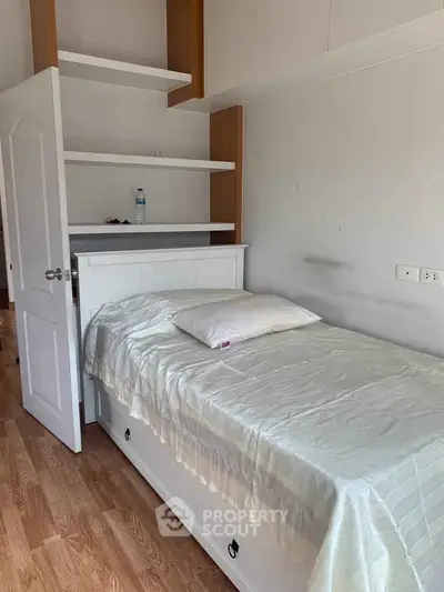 Cozy bedroom with single bed and built-in shelves, perfect for compact living.