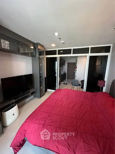 Modern bedroom with red bedding, TV, and glass partition leading to a cozy living area.