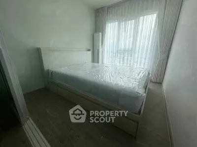 Modern bedroom with large window and minimalist design, featuring a bed with plastic cover and light curtains.