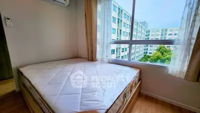 Cozy bedroom with large window offering a stunning view of modern apartment complex.