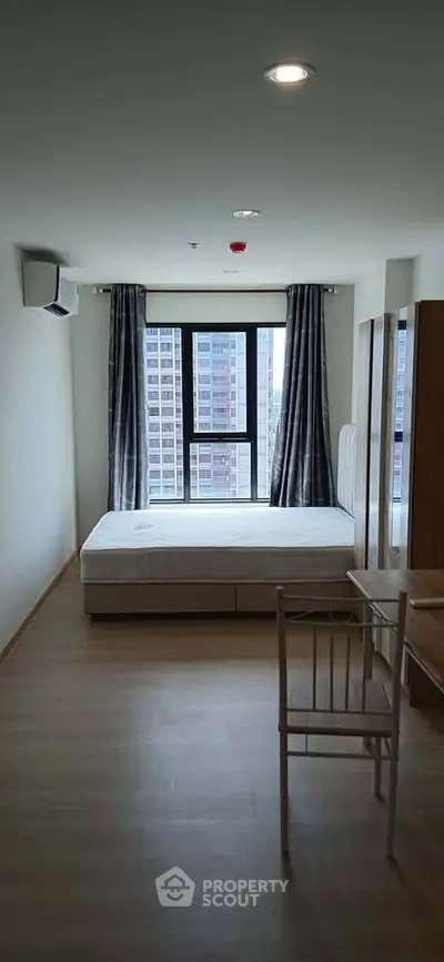 Modern bedroom with large window and minimalist furnishings in urban apartment.