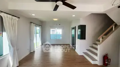 Spacious modern living room with wooden flooring and ceiling fan, featuring large windows for natural light.