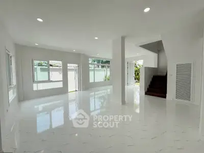 Spacious modern living room with large windows and elegant staircase in a bright open layout.