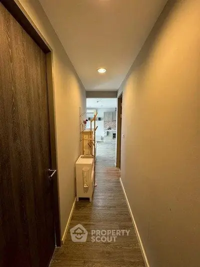 Modern apartment hallway leading to a bright kitchen with wooden flooring.