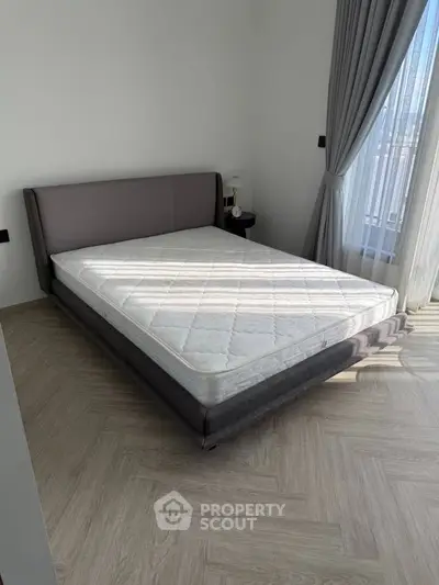 Spacious bedroom with modern bed and natural light through large window.