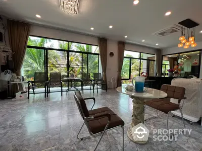 Expansive living room with marble flooring and large windows offering a lush garden view, complemented by modern furniture and elegant lighting fixtures.