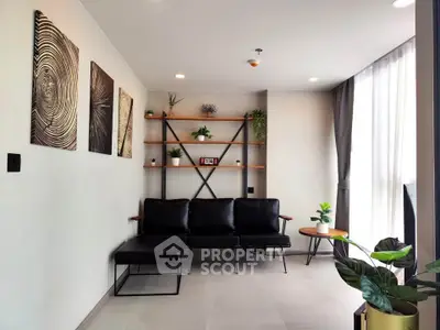 Modern living room with stylish decor and natural light, featuring black leather seating and wall art.
