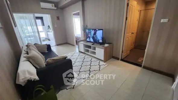 Cozy living room with modern decor and TV, leading to a bright balcony.