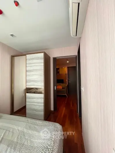 Modern bedroom with wooden flooring and air conditioning, featuring a sleek wardrobe and cozy ambiance.