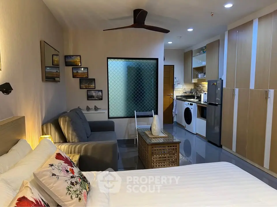 Modern studio apartment with cozy living area and compact kitchen featuring washing machine and fridge.