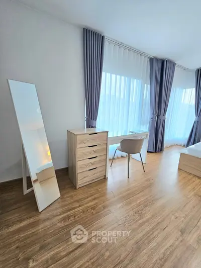 Modern bedroom with wooden flooring, stylish curtains, and elegant furniture including a mirror and dresser.