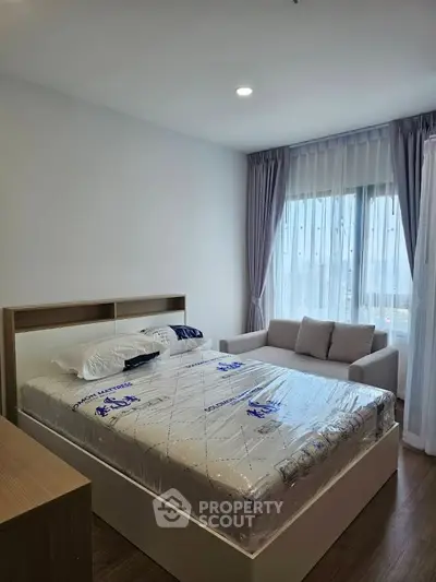 Modern bedroom with cozy bed and stylish sofa, featuring large window with elegant curtains.
