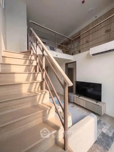 Modern loft apartment with stylish staircase and cozy living area, featuring a sleek TV setup and air conditioning.