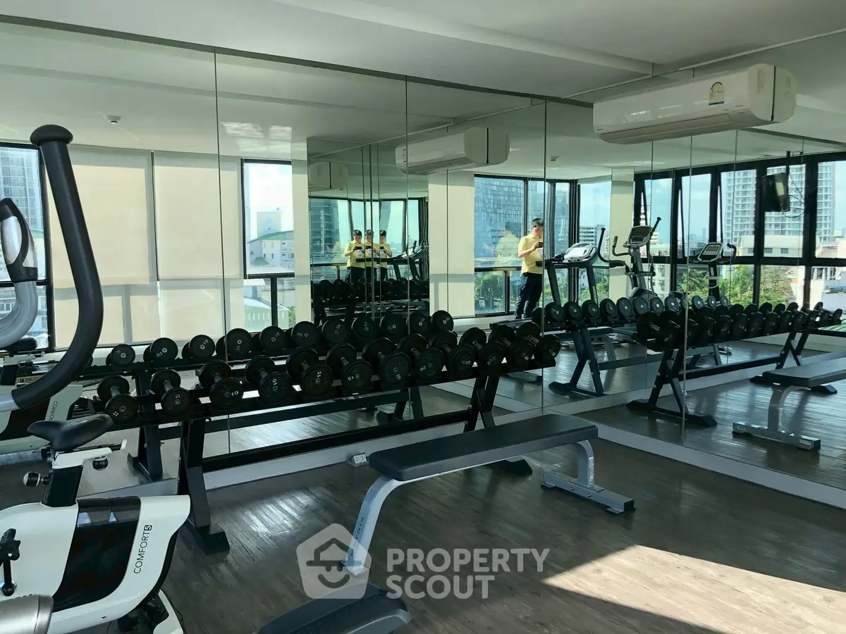 Modern gym with mirrored walls and city view, featuring exercise equipment and weights.