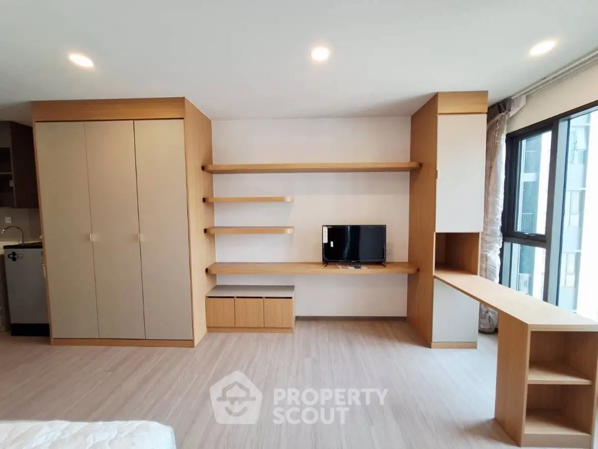 Modern living room with built-in wooden shelves and TV, featuring large windows for natural light.