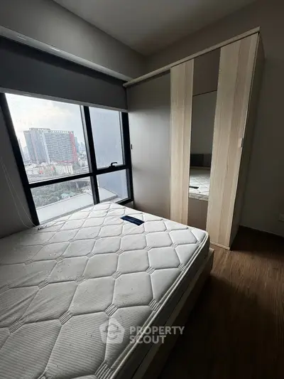 Modern bedroom with city view, featuring a large window and sleek wardrobe.