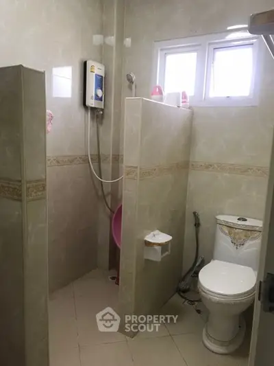 Compact bathroom with shower and toilet, featuring tiled walls and small window.