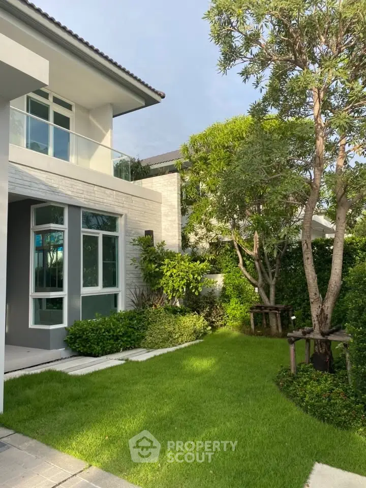 Modern two-story house with lush green garden and large windows, perfect for family living.