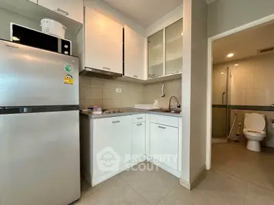 Modern kitchen with sleek white cabinets and stainless steel fridge adjacent to a bathroom.