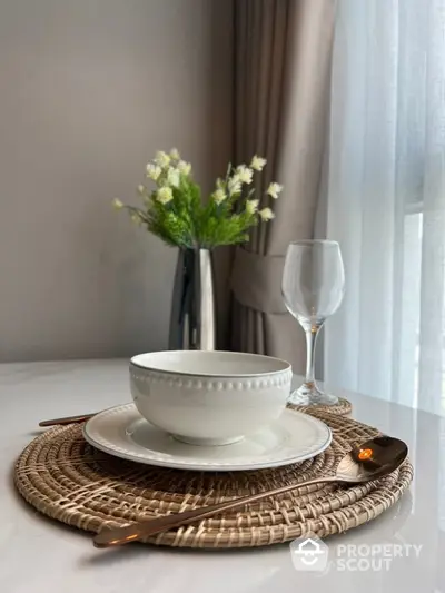 Elegant dining setup with white dishware and glass on woven placemat, perfect for modern interiors.