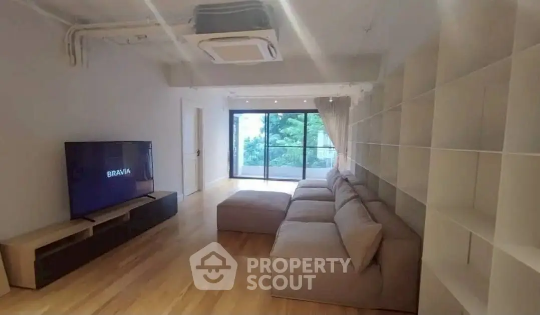 Spacious living room with modern sofa and large TV, featuring a serene balcony view.
