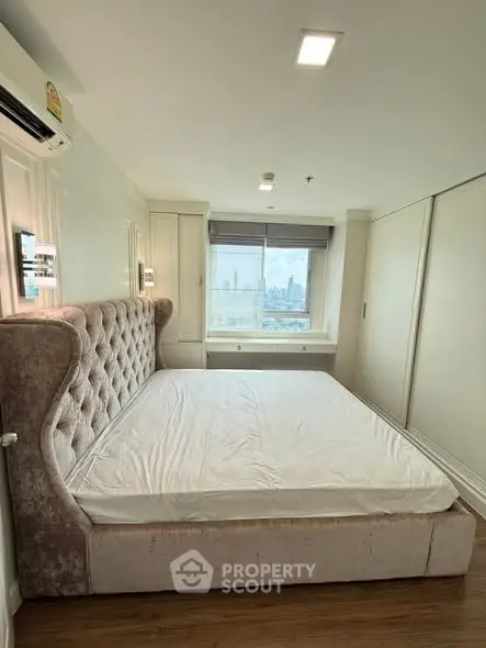 Spacious bedroom with plush bed and city view window, perfect for relaxation.