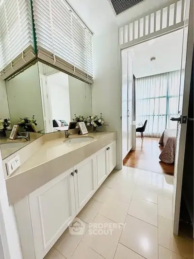 Modern bathroom with sleek vanity leading to a bright bedroom with large windows.