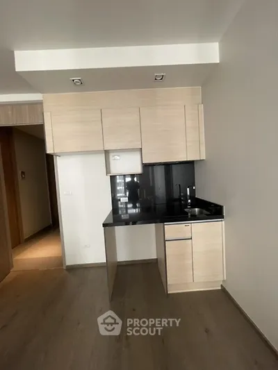 Modern minimalist kitchen with sleek cabinetry and black countertop in open layout apartment.