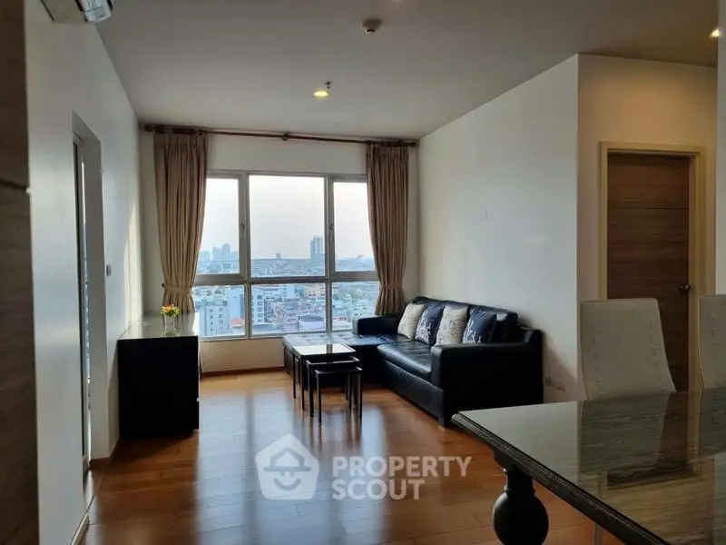 Spacious living room with city view, modern furniture, and natural light in a high-rise apartment.