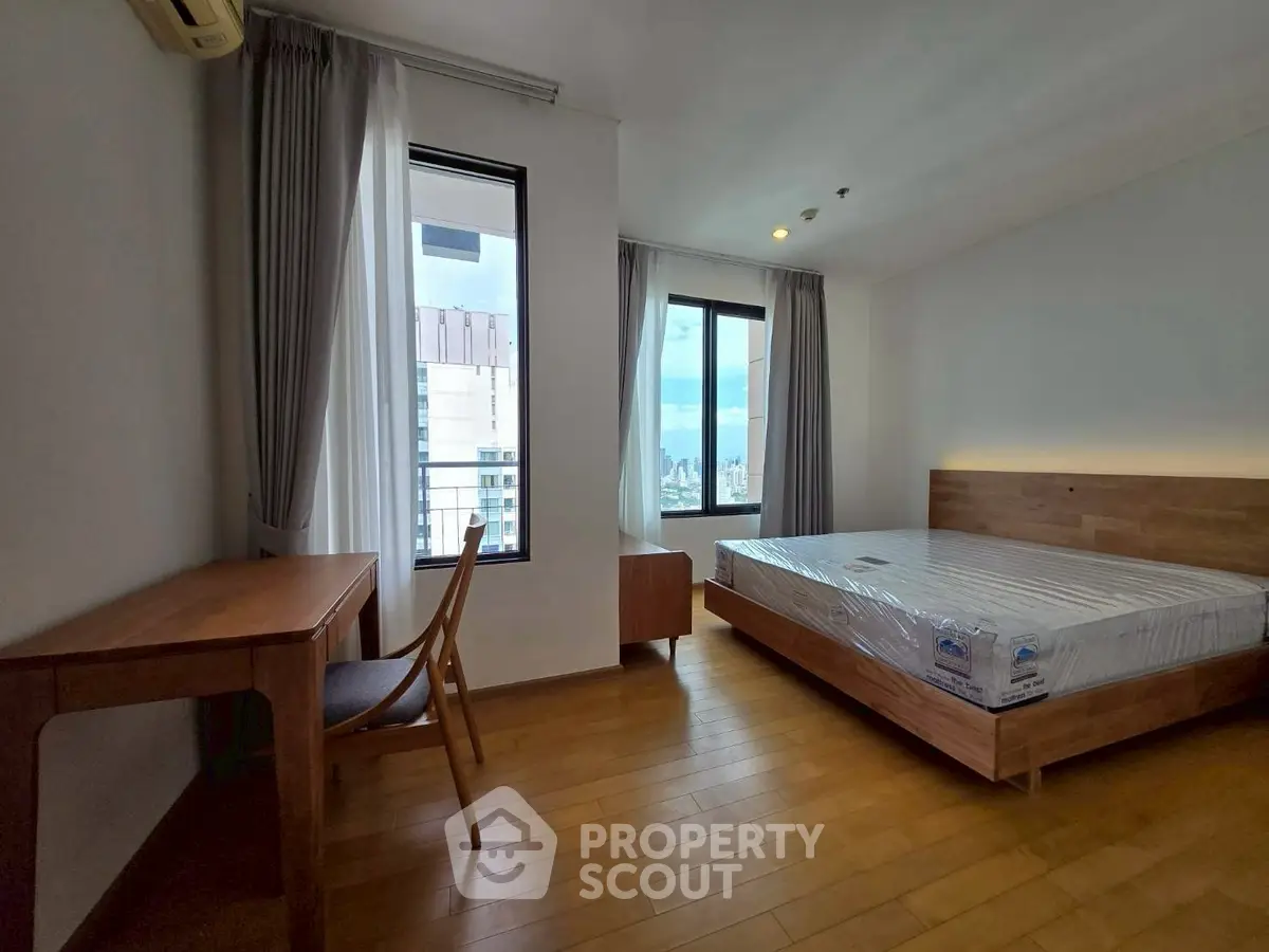 Spacious bedroom with wooden flooring and city view balcony in modern apartment