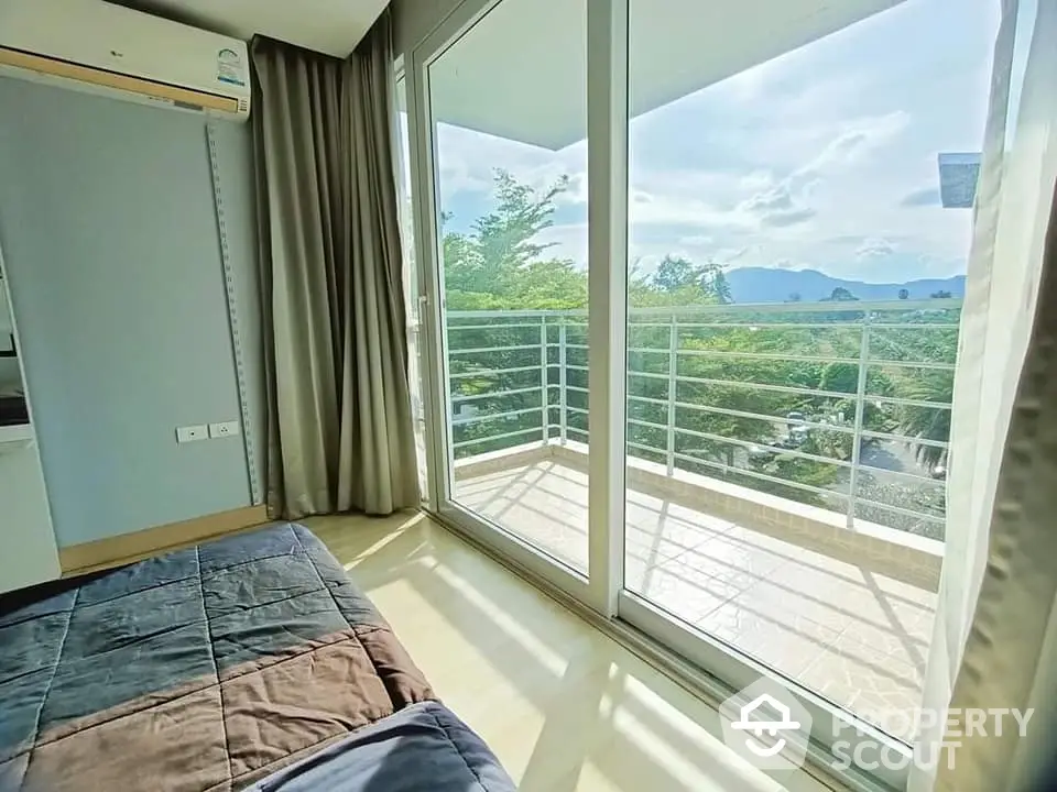 Bright bedroom with balcony and stunning view of lush greenery and mountains.