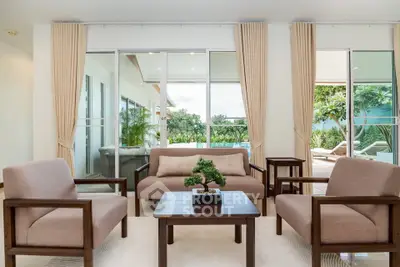 Elegant living room with modern furniture and large windows overlooking a lush garden and pool area.